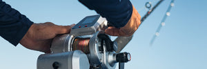 Person using an electronic PENN Fathom fishing reel with a clear blue sky background