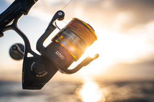 PENN Battle IV Spinning Fishing Reel in black and gold, with an orange line, set against a blurred sunset over the water