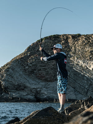 Man casting from a rocky shoreline into the sea with cliffs in the background