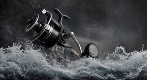 A black and white picture of a PENN Pursuit V Spinning reel sitting on a rock with sea waves crashing around it, set on a dark background