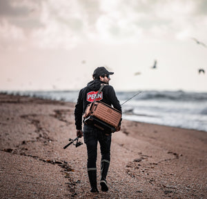 Foucauld walking along a beach with a PENN Conflict Elite Rod and fishing bag, wearing a Penn hoodie. 