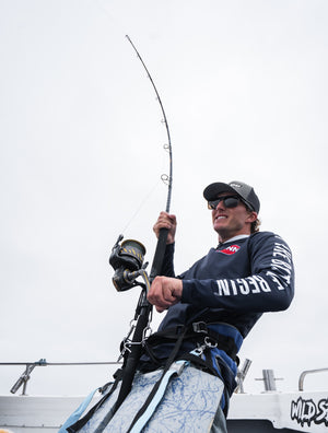 Male PENN fisherman with a near vertical rod under strain, reeling in with a sky background