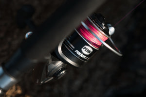 Close-up of a PENN Pursuit V fishing reel with pink line on a dark background
