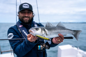 PENN Angler holding a sea bass on a boat with rods and ocean in the background